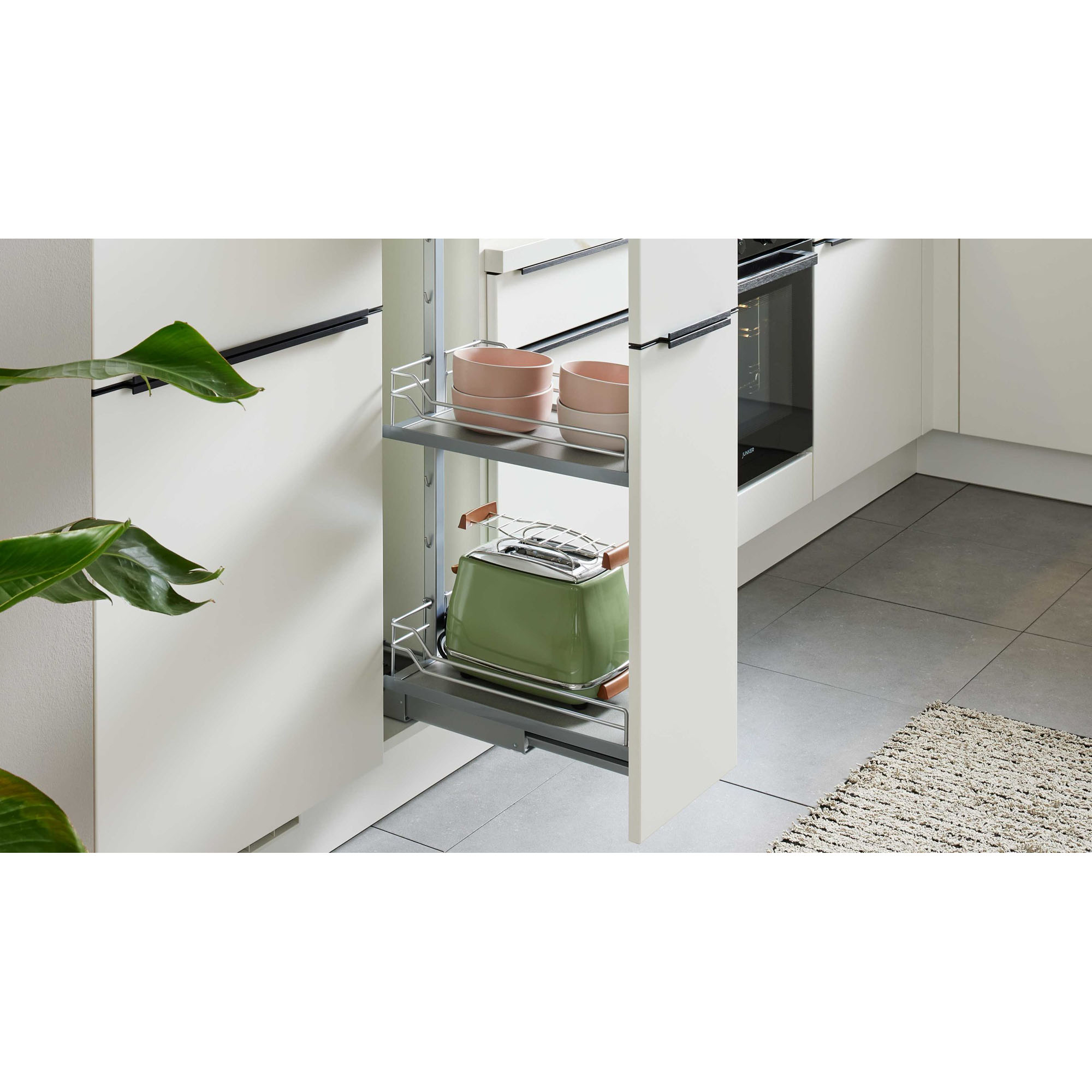 Geöffneter Auszugsschrank in einer weißen Küche mit grünem Toaster auf der unteren Ebene und rosa Schalen auf der oberen Ablage