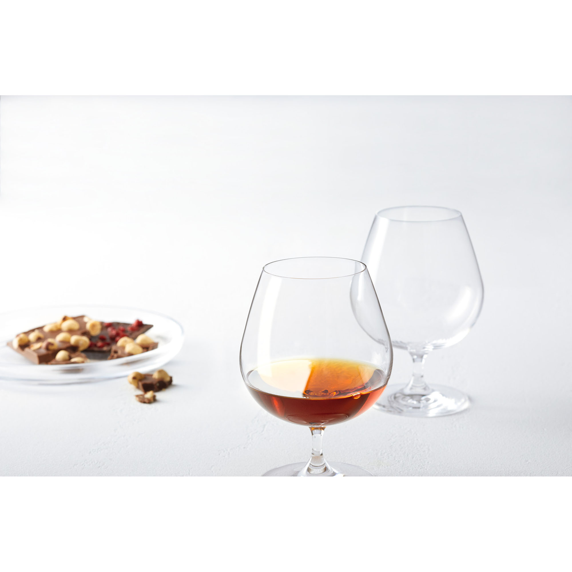 Cognacglas mit bernsteinfarbenem Getränk und zweitem leeren Glas im Hintergrund