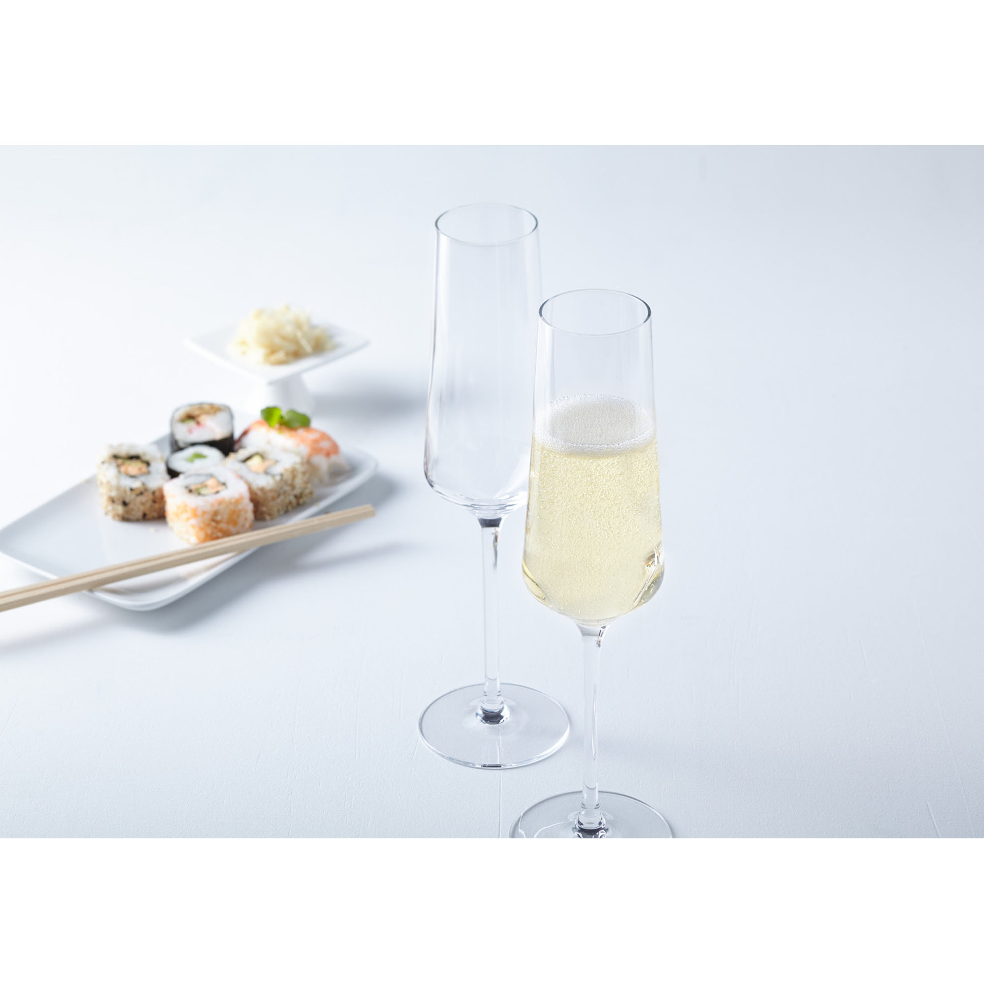 Zwei Sektgläser eines gefüllt mit Schaumwein neben Sushi auf hellem Tisch
