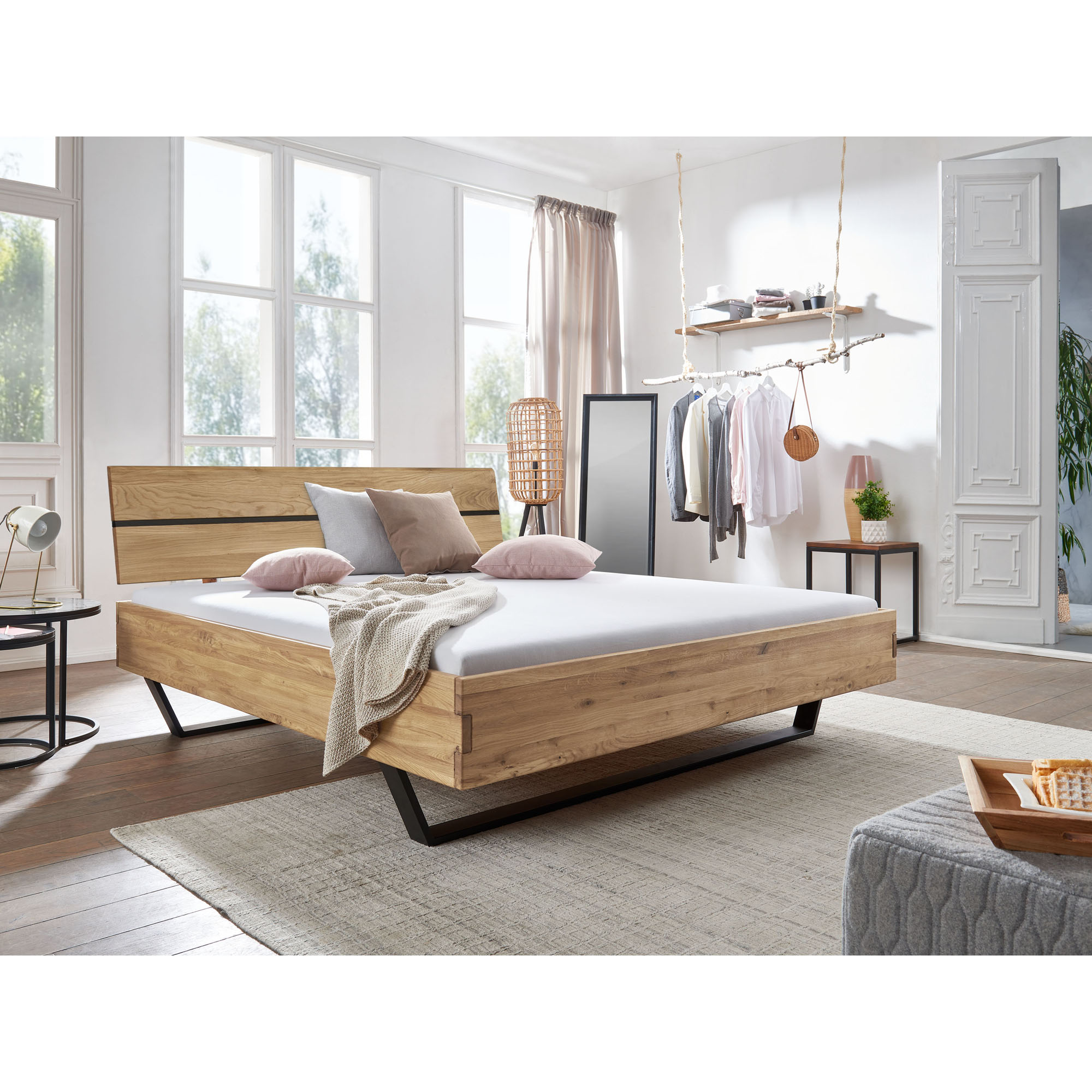 Doppelbett aus Holz mit schwarzem Metallgestell in einem hellen Schlafzimmer mit Fenster und Möbeln