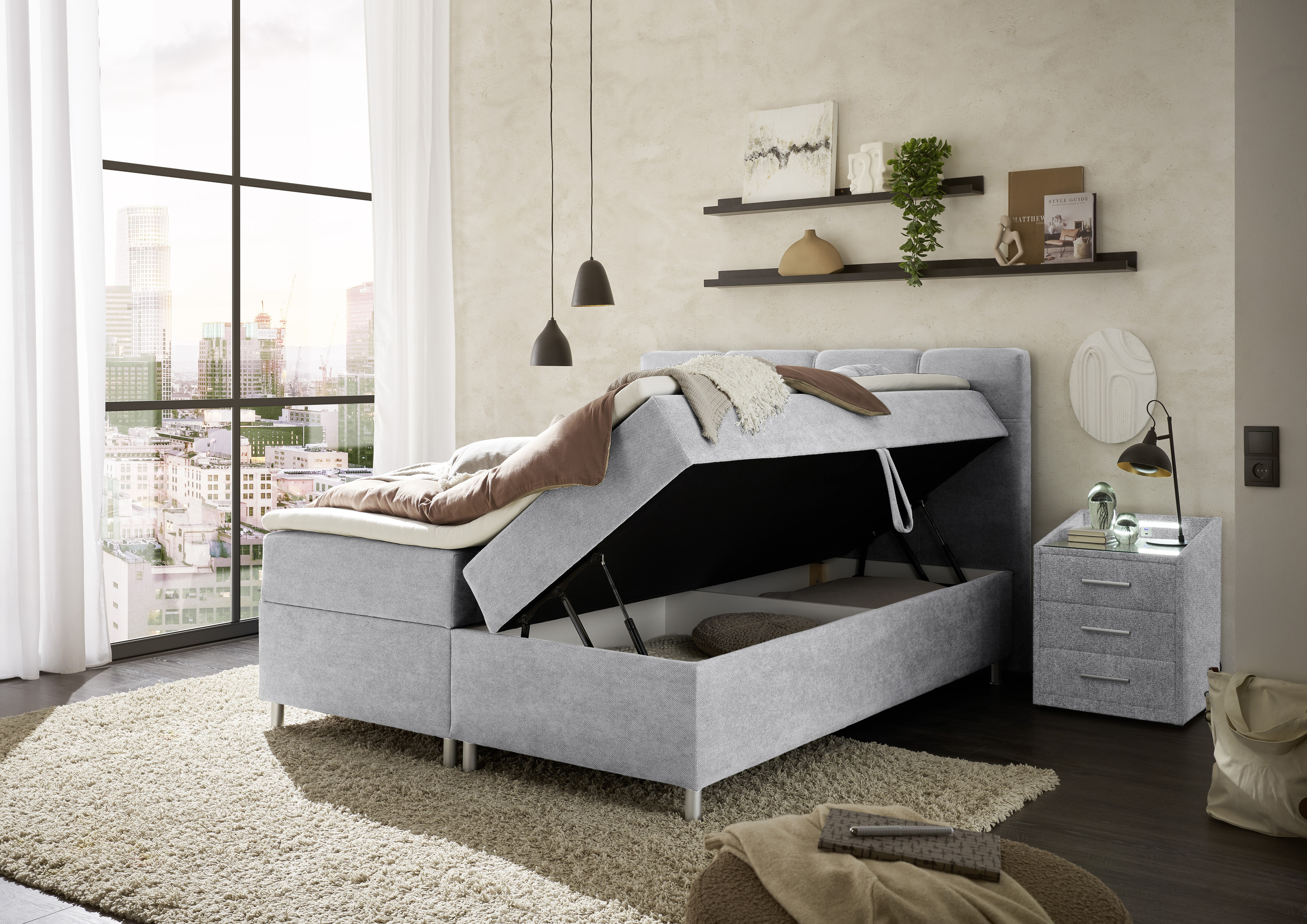 Boxspringbett „Curio 80 Silver“ in einem eingerichteten Schlafzimmer, Bettkasten geöffnet, Stauraum erkennbar, dekoriert mit Decke und Kissen