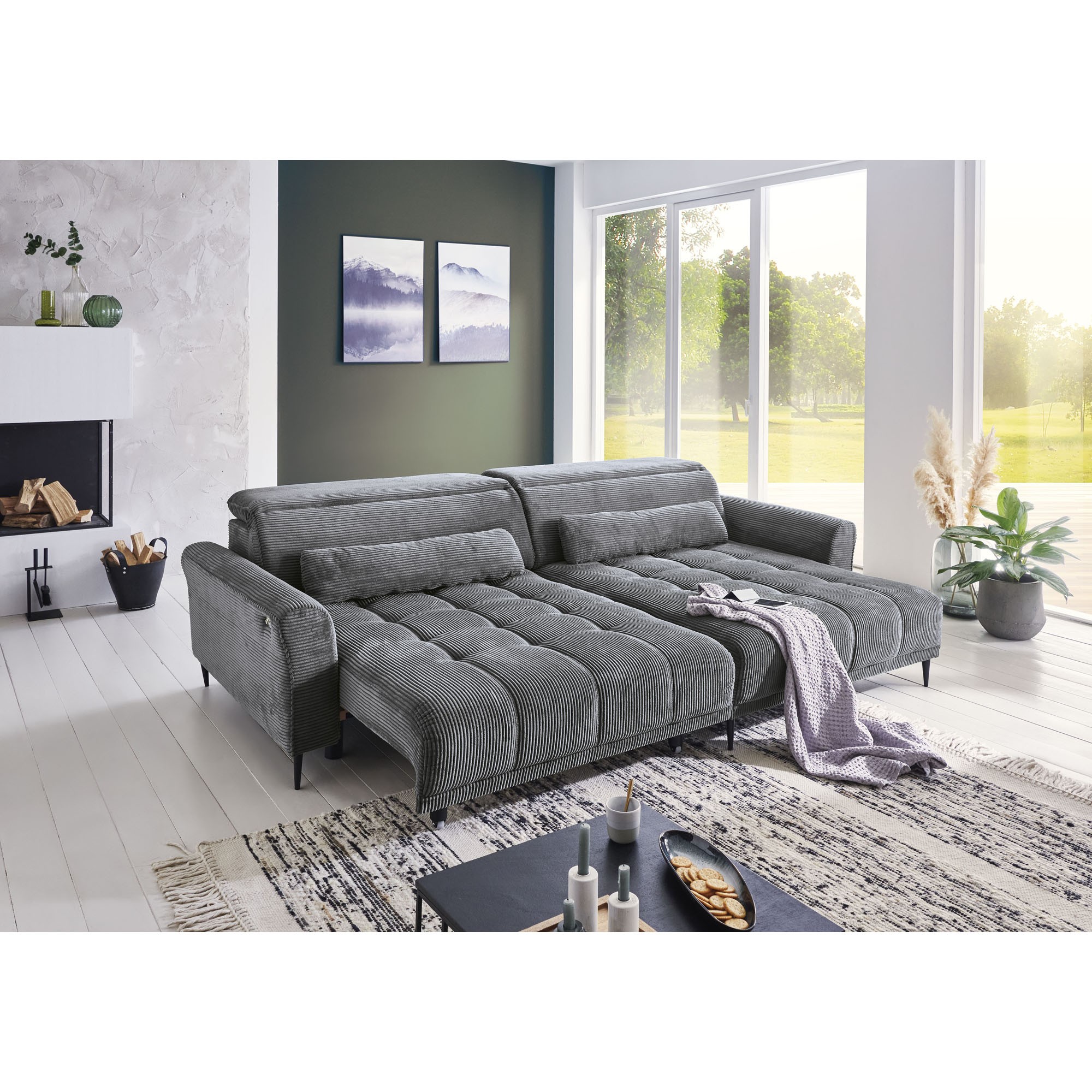 Helles Wohnzimmer mit modernem Ecksofa in grauem Cordstoff und großen Fenstern im Hintergrund.