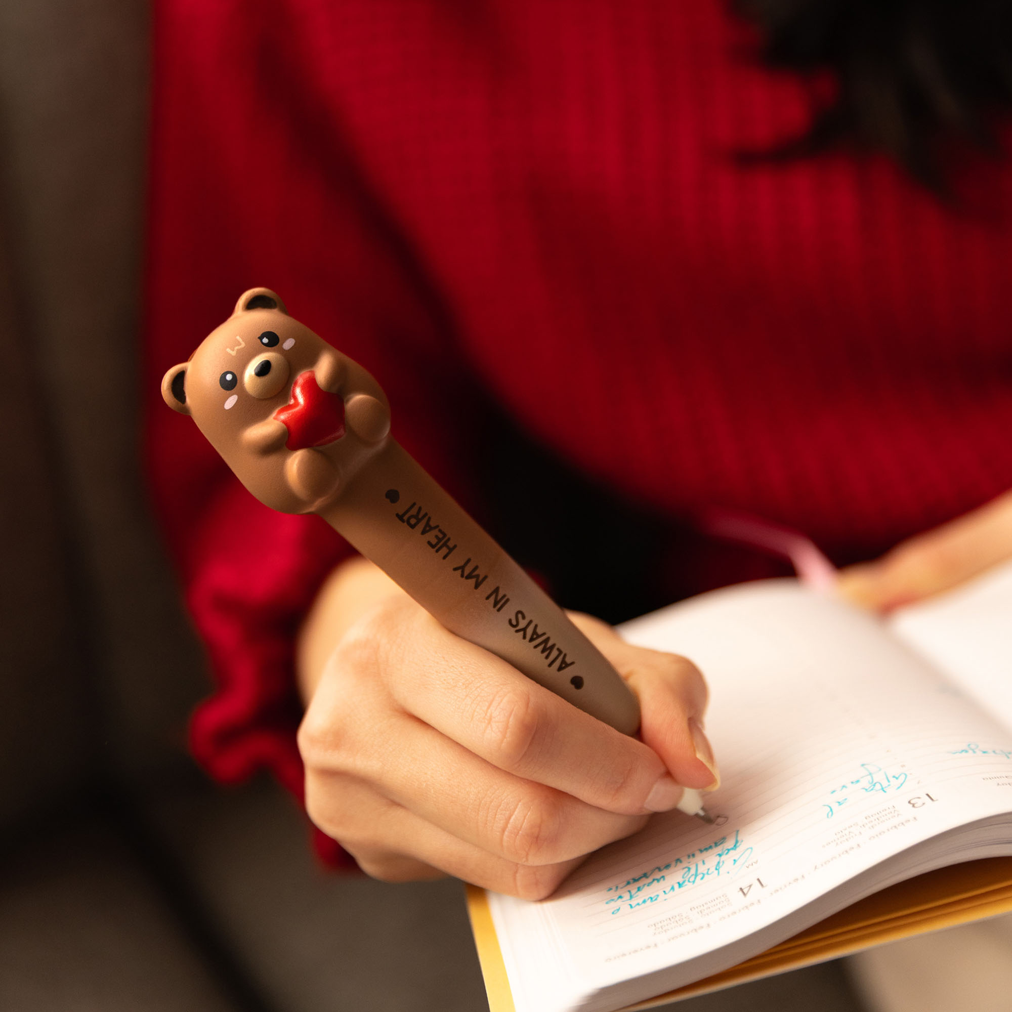 Brauner Gelstift mit Teddybär-Aufsatz, von einer Person beim Schreiben in einem Notizbuch verwendet.