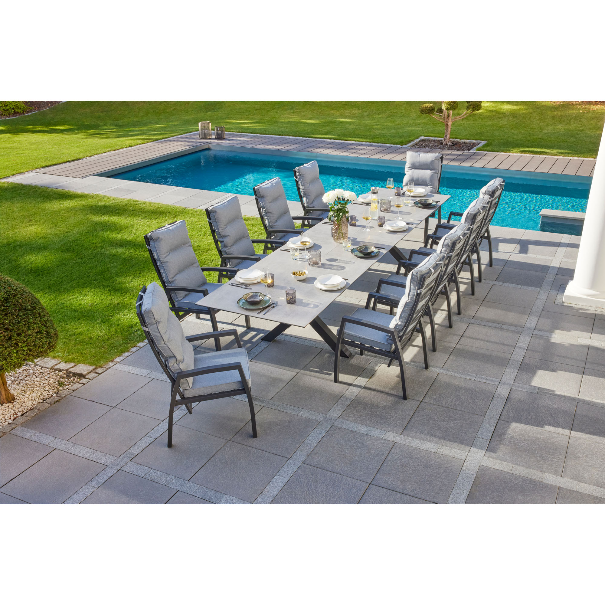 Mehrere Gartenstühle mit Polstern stehen um einen rechteckigen Tisch auf einer Terrasse neben einem Pool