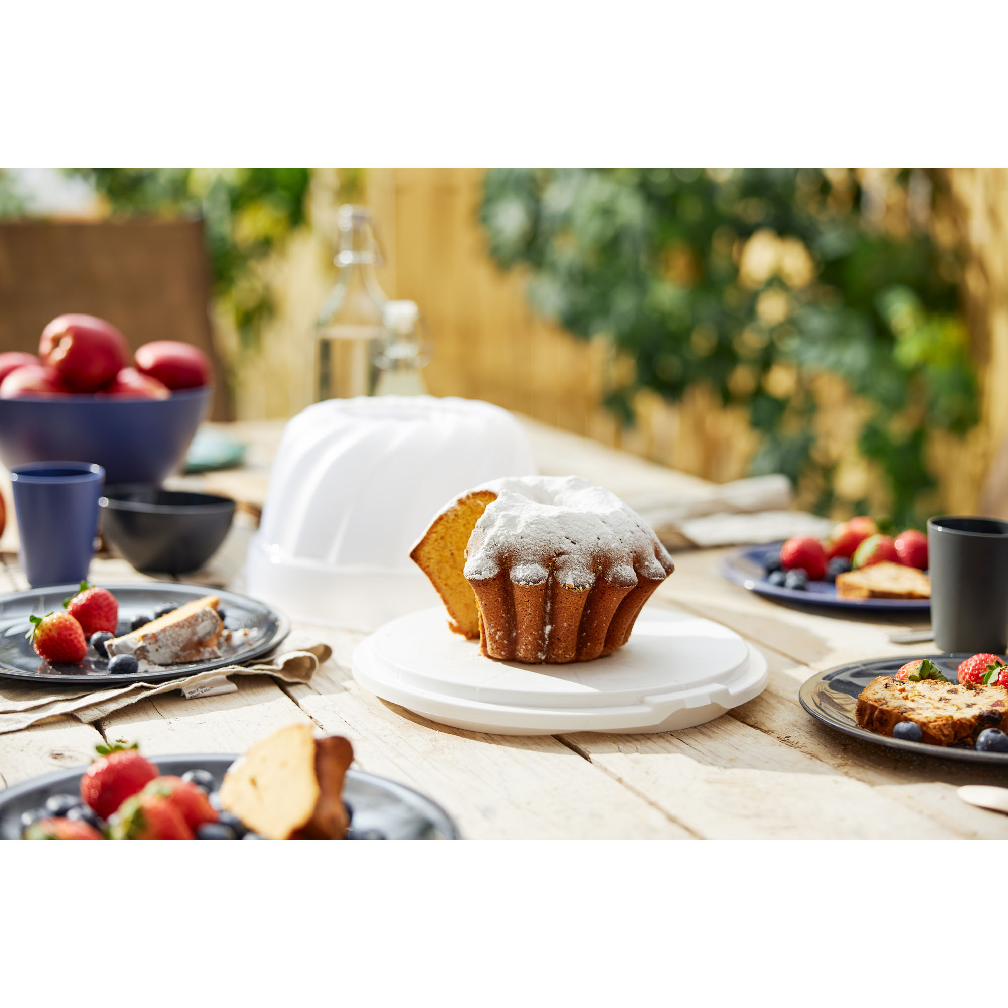 Transparente Tortenhaube über einem Kuchen auf einem gedeckten Tisch im Außenbereich