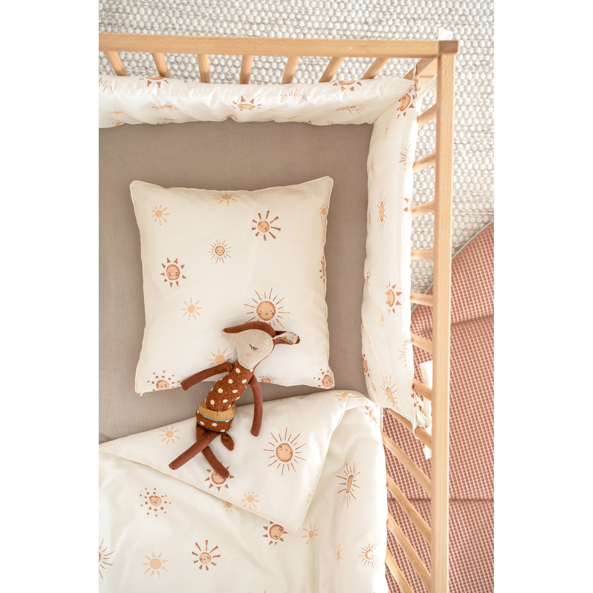 Cremefarbenes Bettnestchen mit Sonnendruck in einem Holz-Babybett, dazu passende Bettwäsche und ein braunes Stofftier