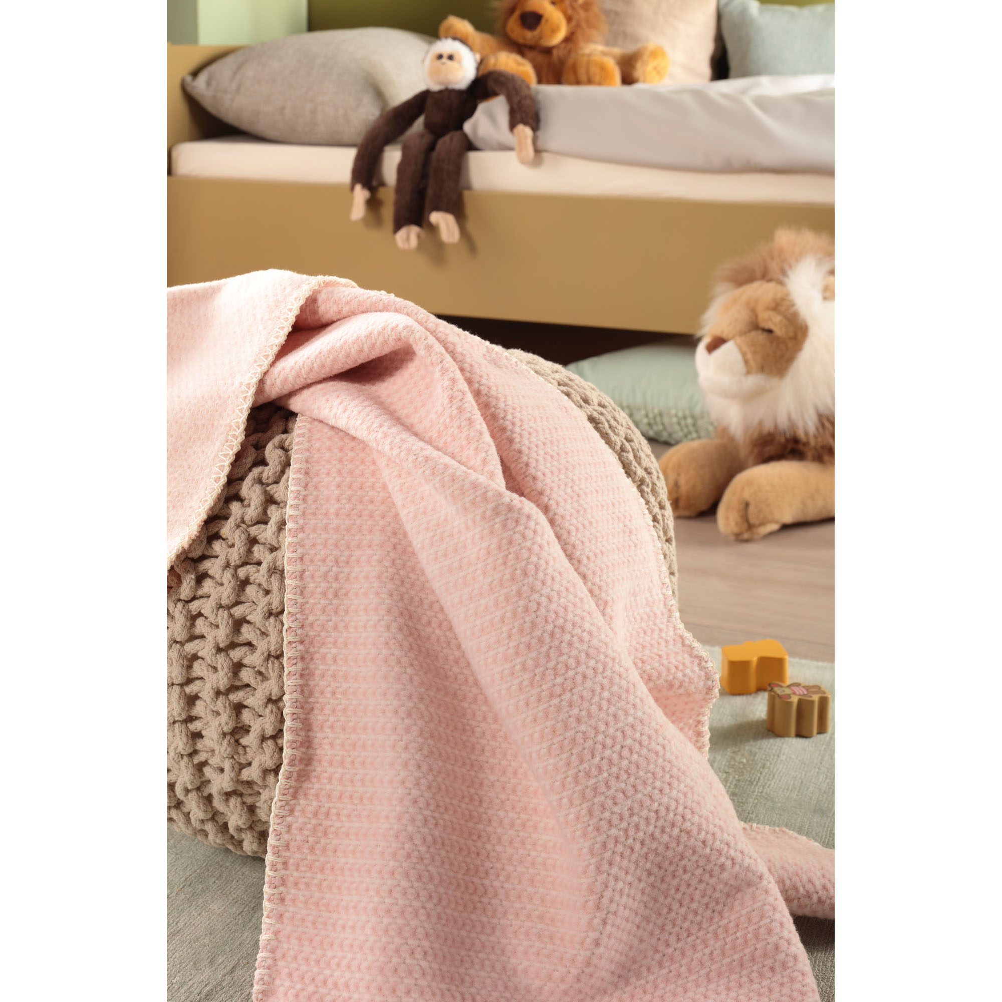 Babydecke Cotton rose liegt in einem Kinderzimmer über einem Möbelstück; Stofftiere und Spielzeug stehen im Hintergrund.