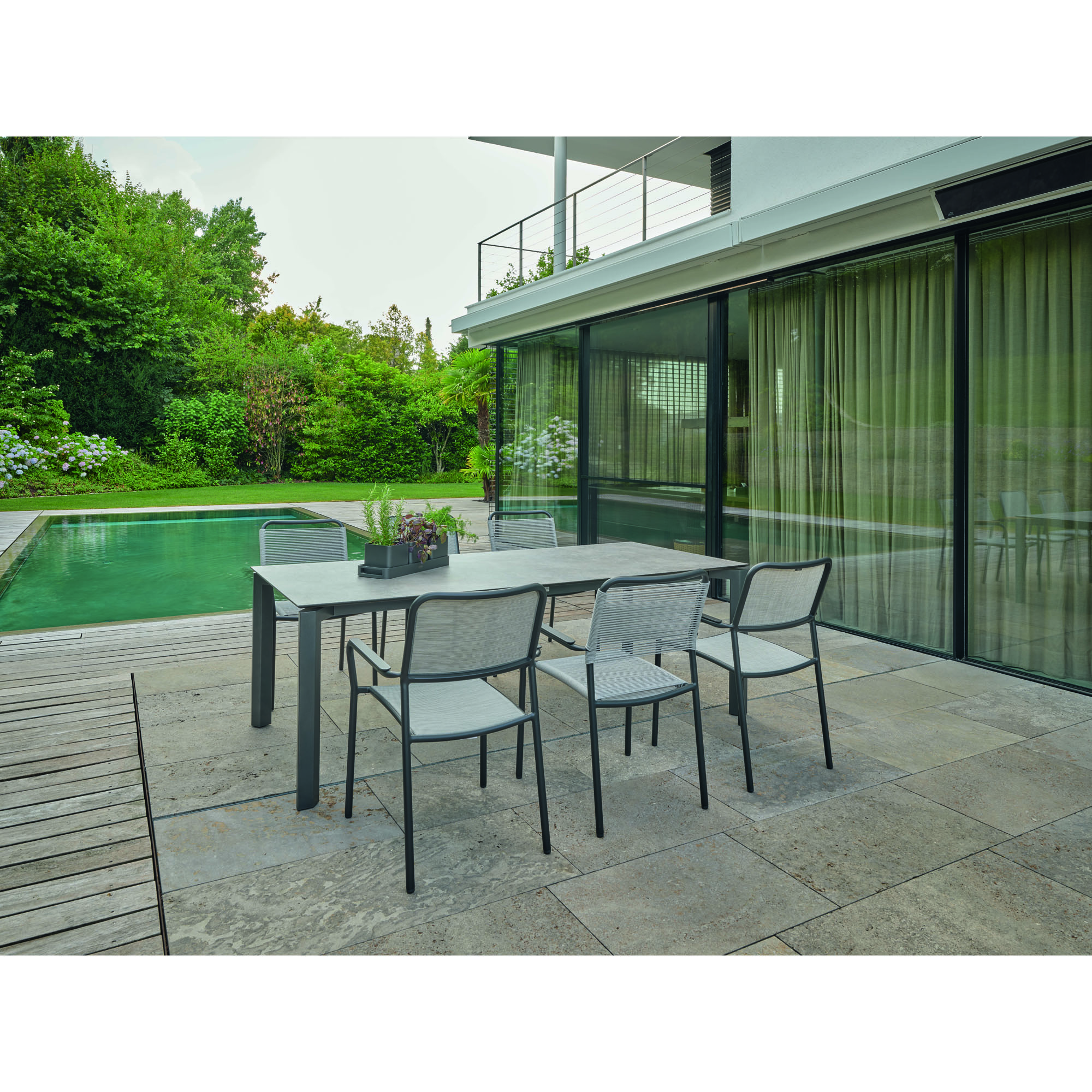 Mehrere Gartenstühle mit Armlehnen an einem rechteckigen Tisch auf einer Terrasse neben einem Pool
