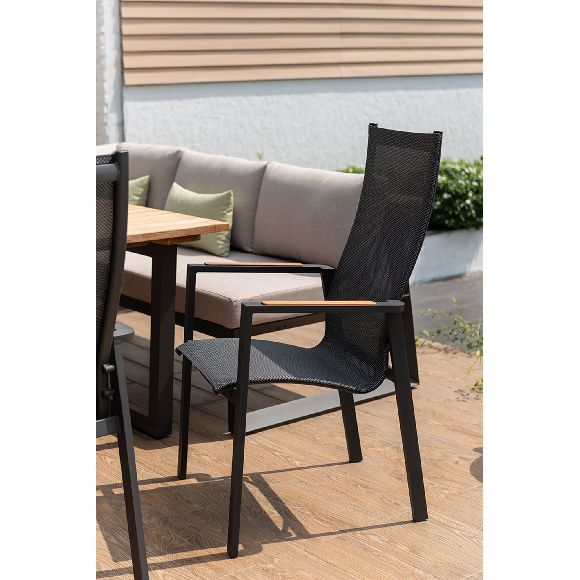 Gartenstuhl mit hoher Rückenlehne und Armlehnen an einem Tisch, dahinter gepolsterte Gartenbank auf einer Terrasse