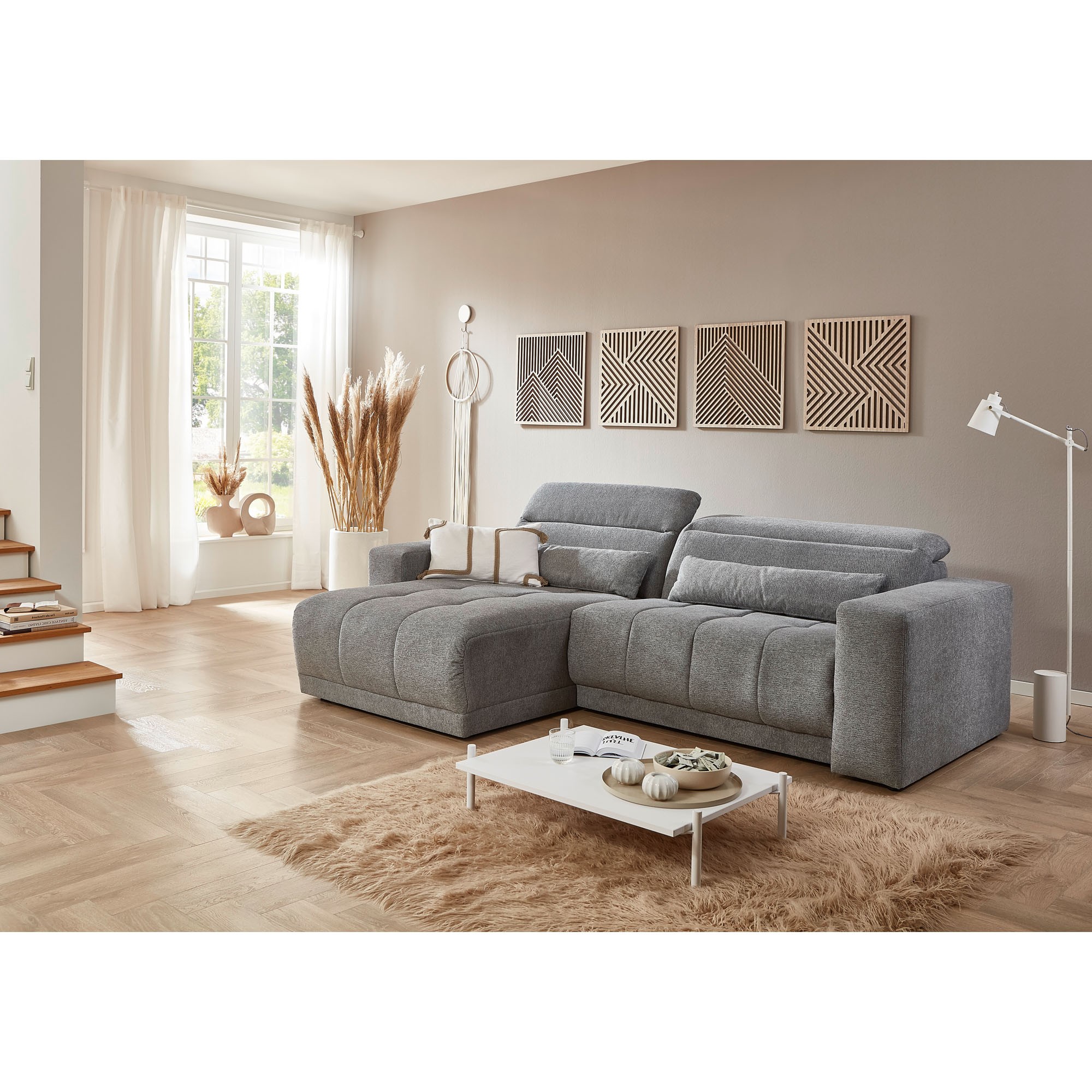 Graues Sofa vor heller Wand mit Holzdekorbildern, Teppich und Tisch im modernen Wohnraum