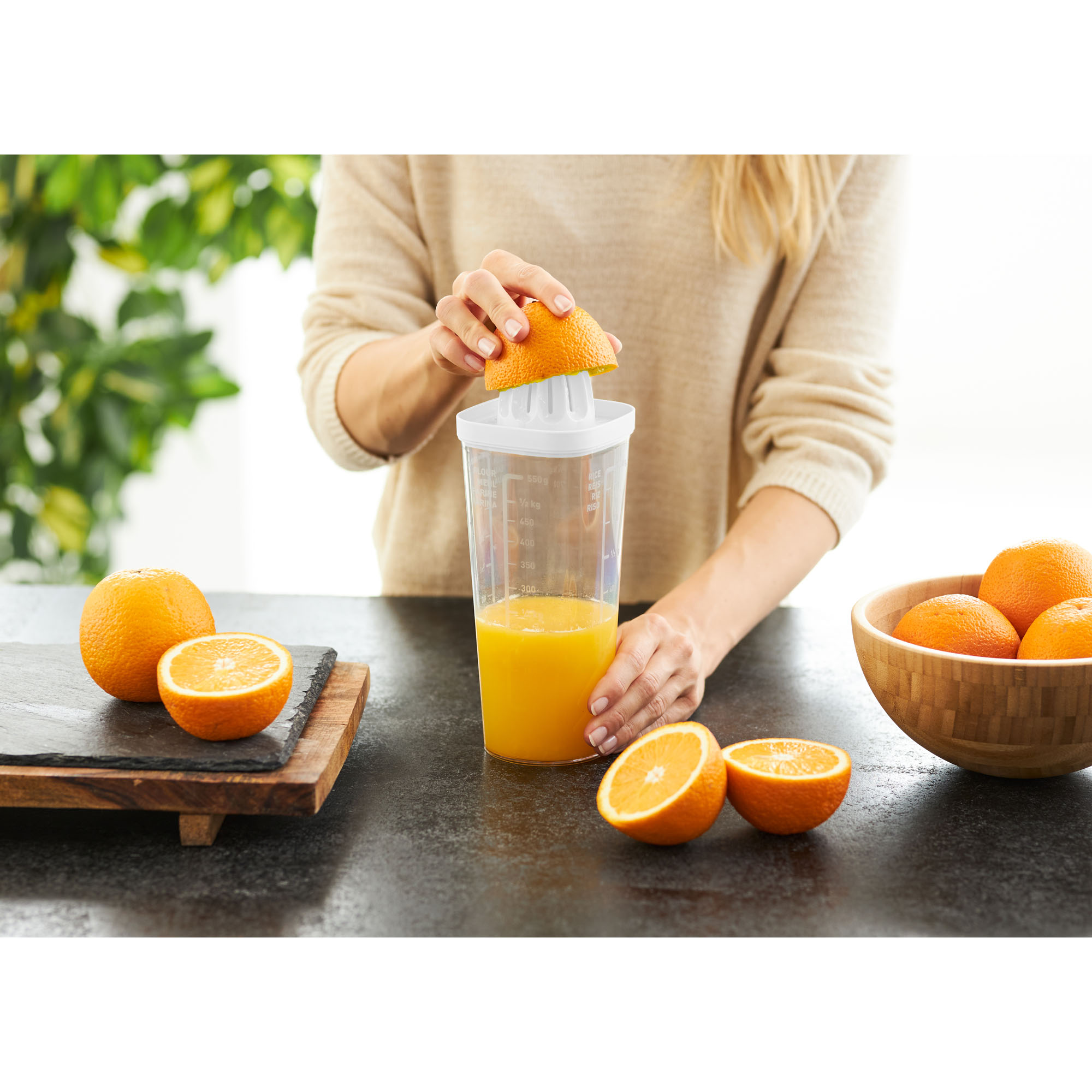 Transparenter Shaker mit Zitruspresse bei der Zubereitung von Orangensaft auf einer Küchenarbeitsplatte