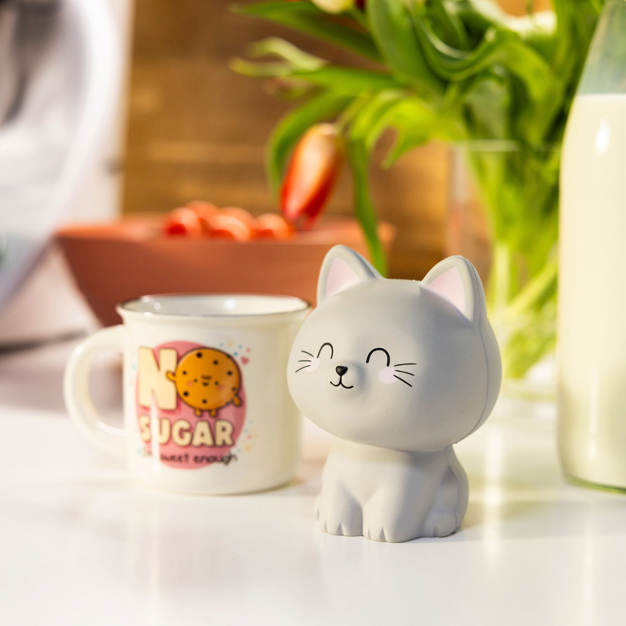 Graue Antistress-Figur in Katzenform, neben einer Tasse und einer Pflanze auf einem Tisch dargestellt.