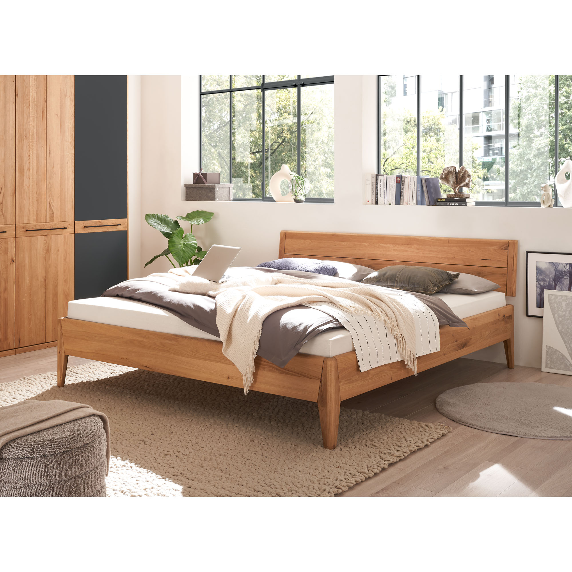 Bett aus Holz in einem Schlafzimmer mit Kleiderschrank und weiteren Möbeln aus Holz
