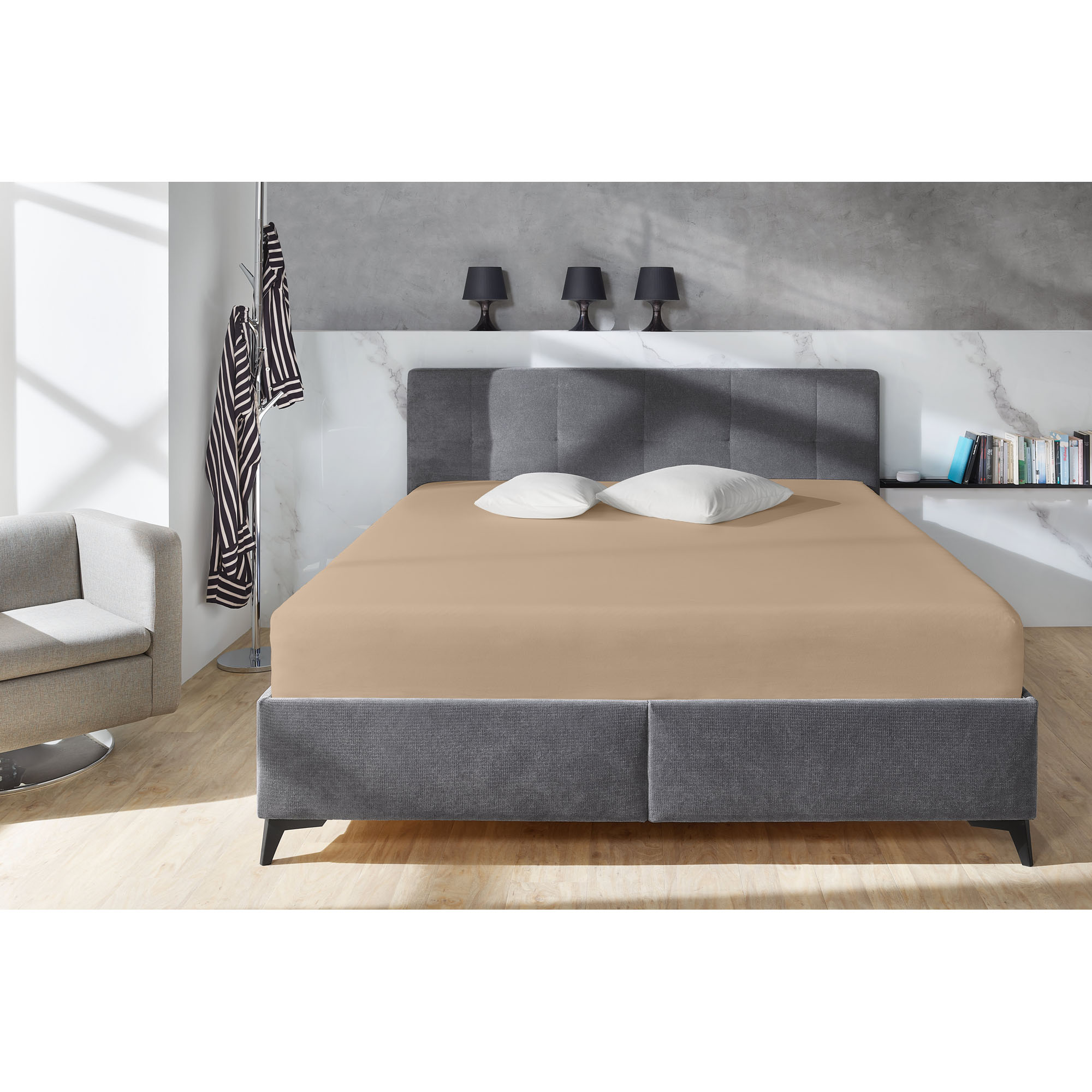 Boxspring-Spannbetttuch in Kiesel auf einem grauen Boxspringbett in einem Schlafzimmer; zwei helle Kissen liegen am Kopfende; Größe 150 x 200 x 38 cm.
