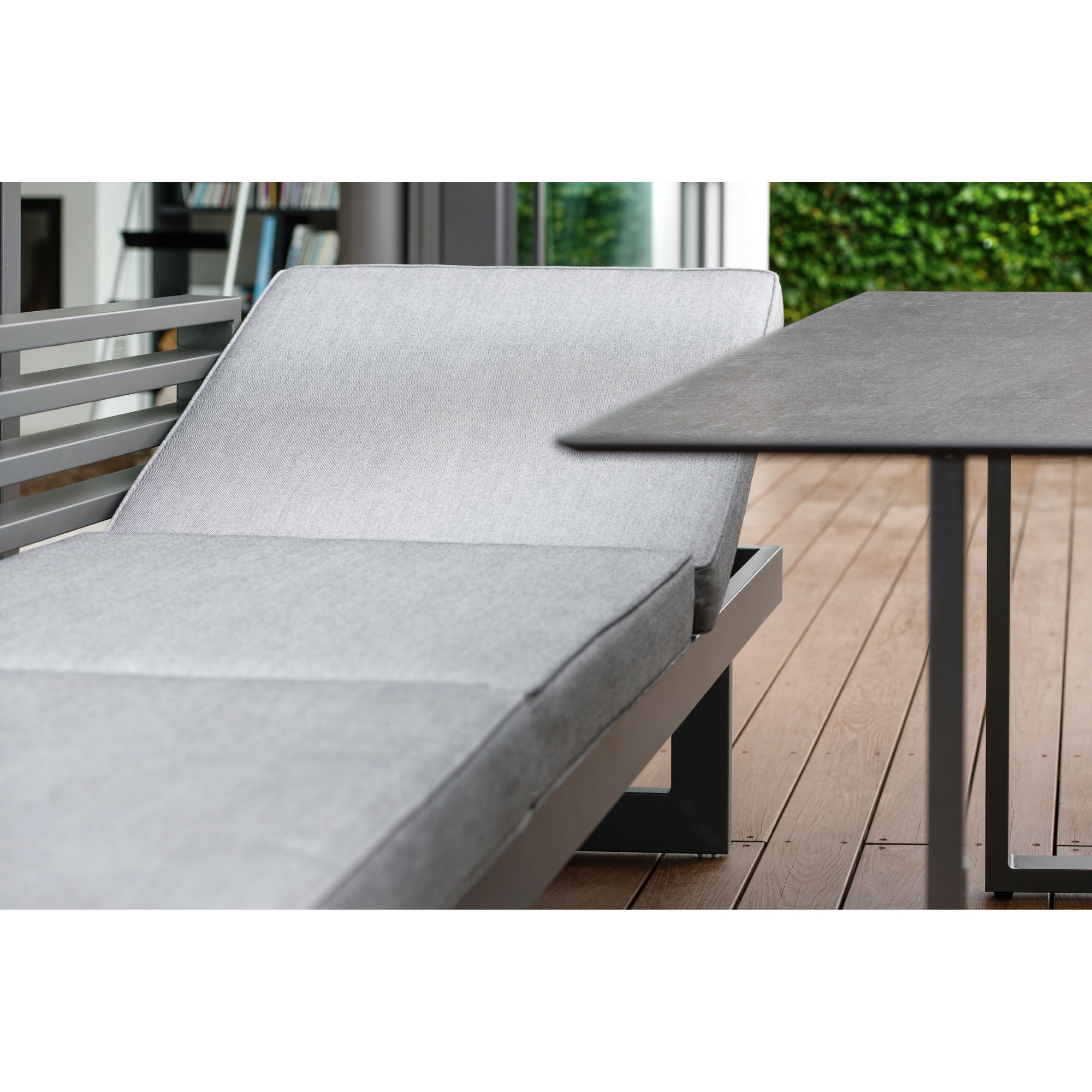 Nahaufnahme einer grauen Gartenbank mit verstellbarer Rückenlehne, die an einem Tisch auf einer Holzterrasse steht.
