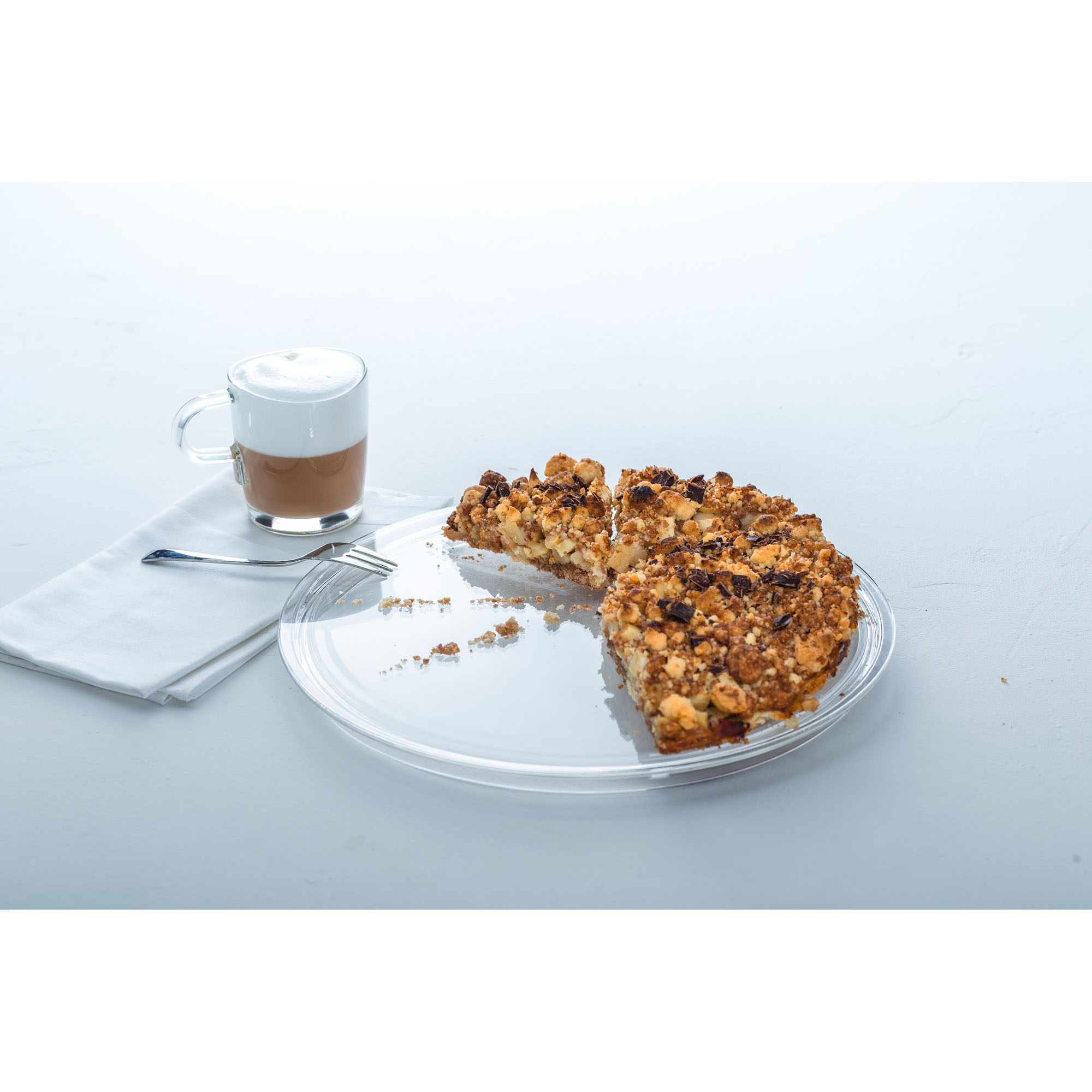 Runde Glasplatte mit Kuchenstück und Tasse Kaffee auf hellem Tisch angerichtet