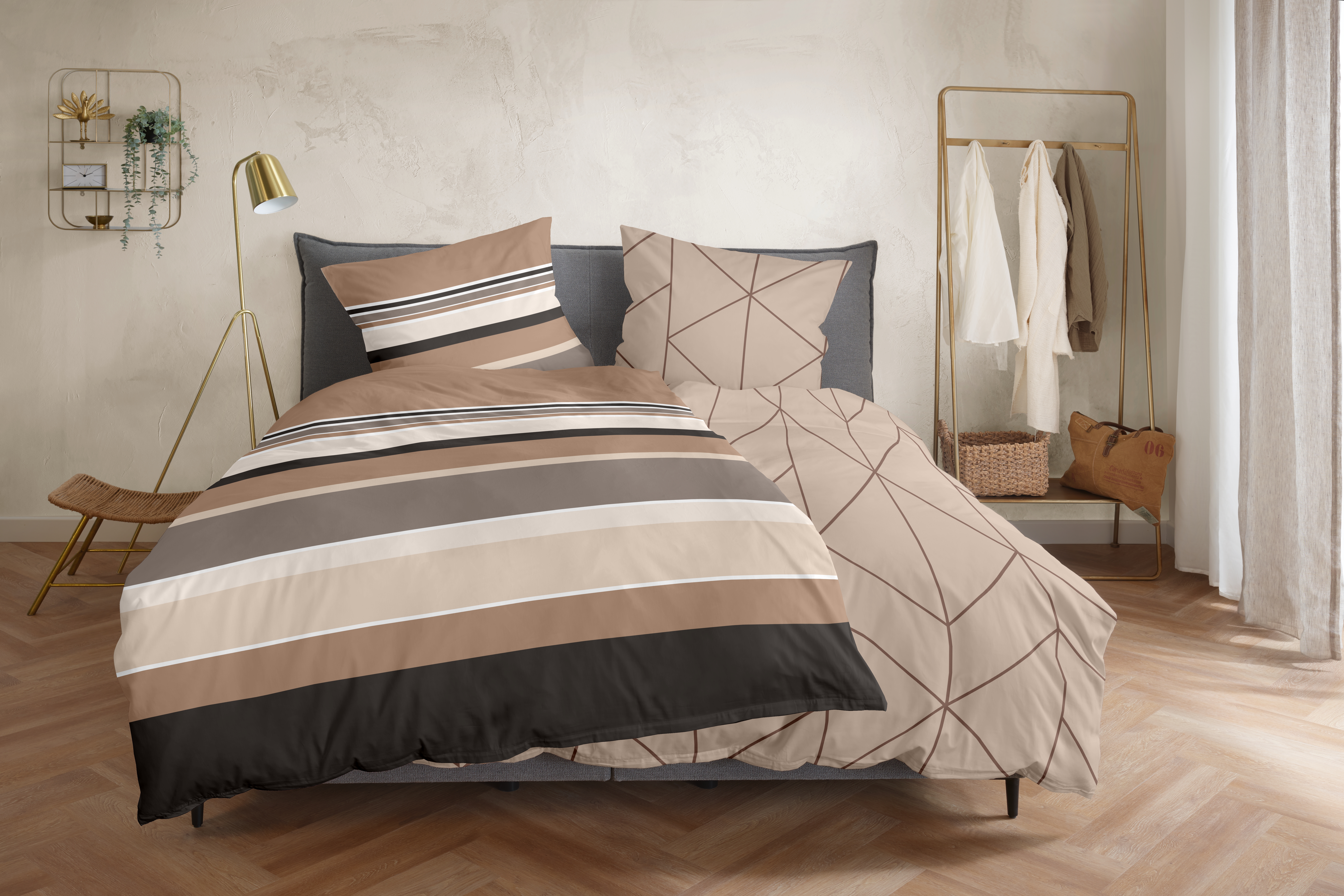 Bett mit braun-grau gestreifter Bettwäsche; ein geometrisch gemustertes Kissen und die abweichende Wendeseite sind sichtbar; Größe 135 x 200 cm.
