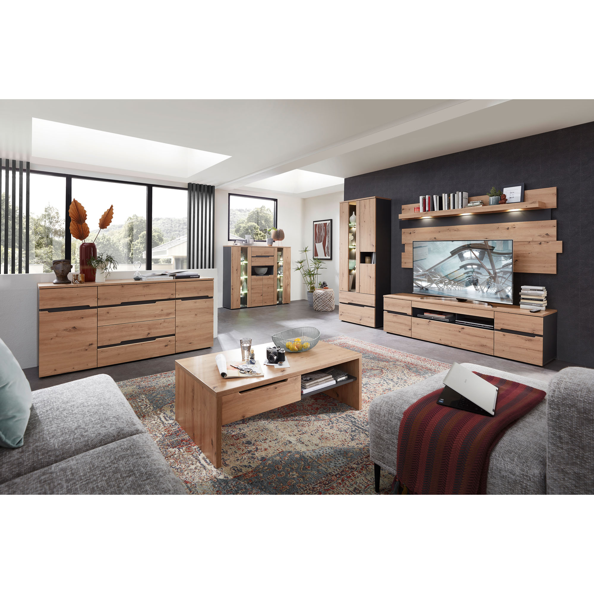 Großes Wohnzimmer mit Sideboard links, Vitrinen mit Beleuchtung im Hintergrund, TV-Wand rechts und einem Holzcouchtisch in der Mitte