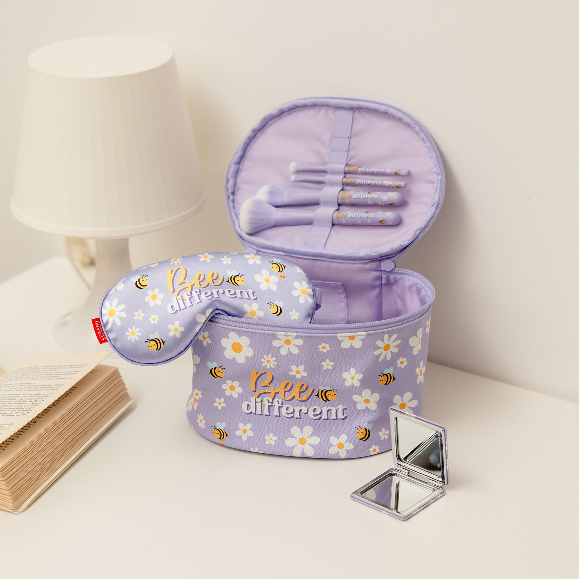 Vier lilafarbene Make-up-Pinsel im Bienen-Design, neben einem geöffneten runden Kosmetikkoffer in einer Wohnszene gezeigt.