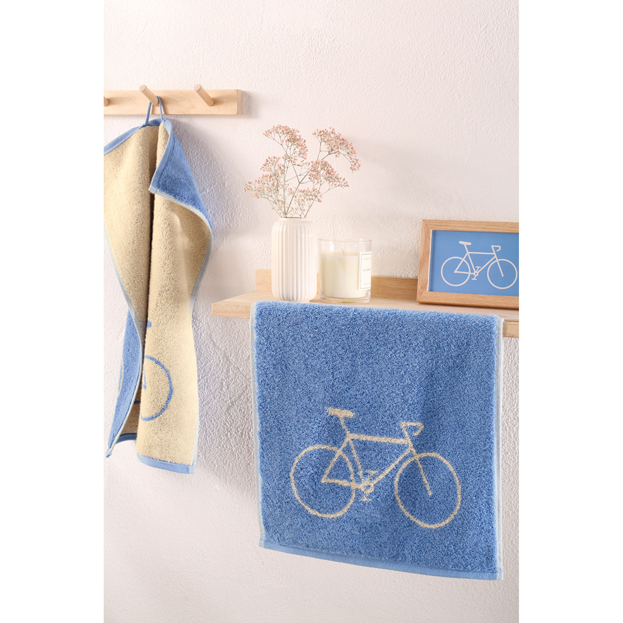 Blaues Gästetuch mit Fahrradmotiv hängt an einem hellen Waschplatz; im Hintergrund ist ein weiteres Tuch mit Fahrradzeichnung.