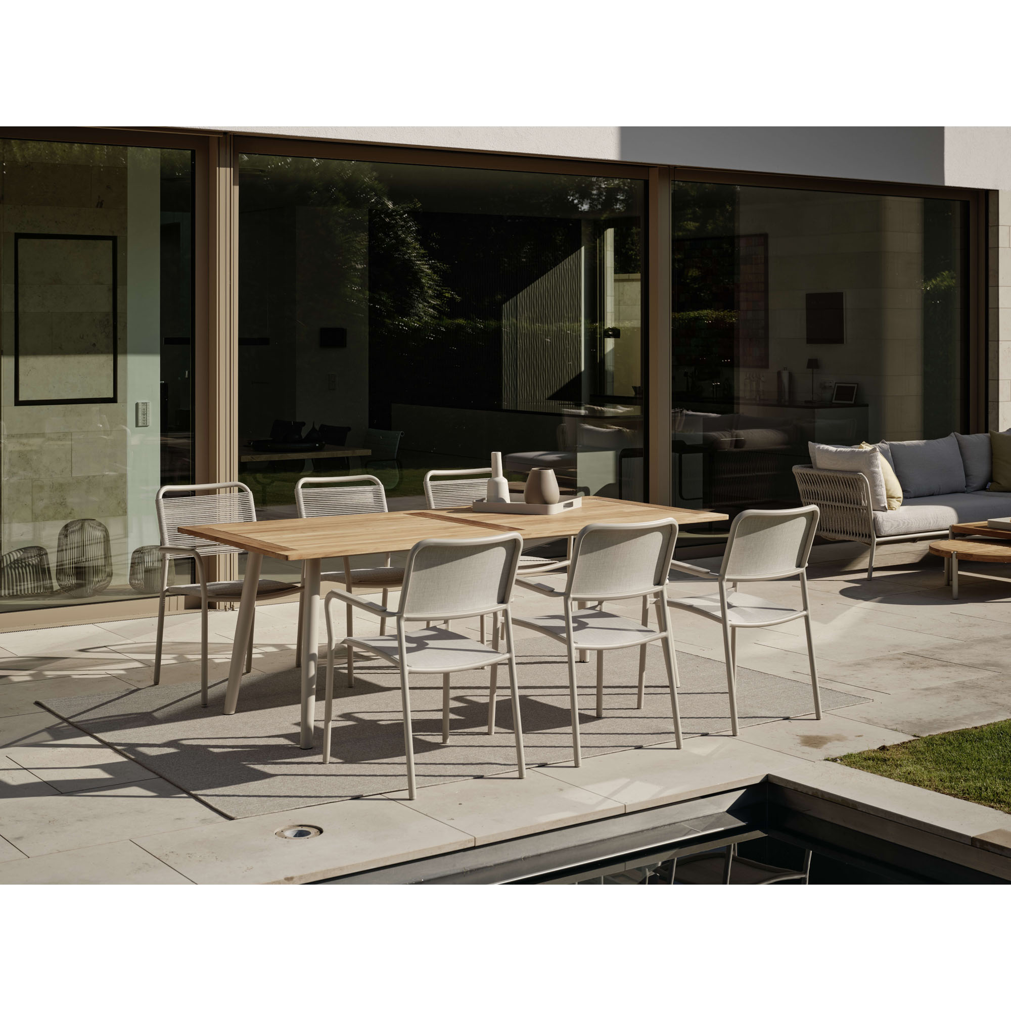 Mehrere Gartenstühle an rechteckigem Tisch auf moderner Terrasse vor Glasfassade
