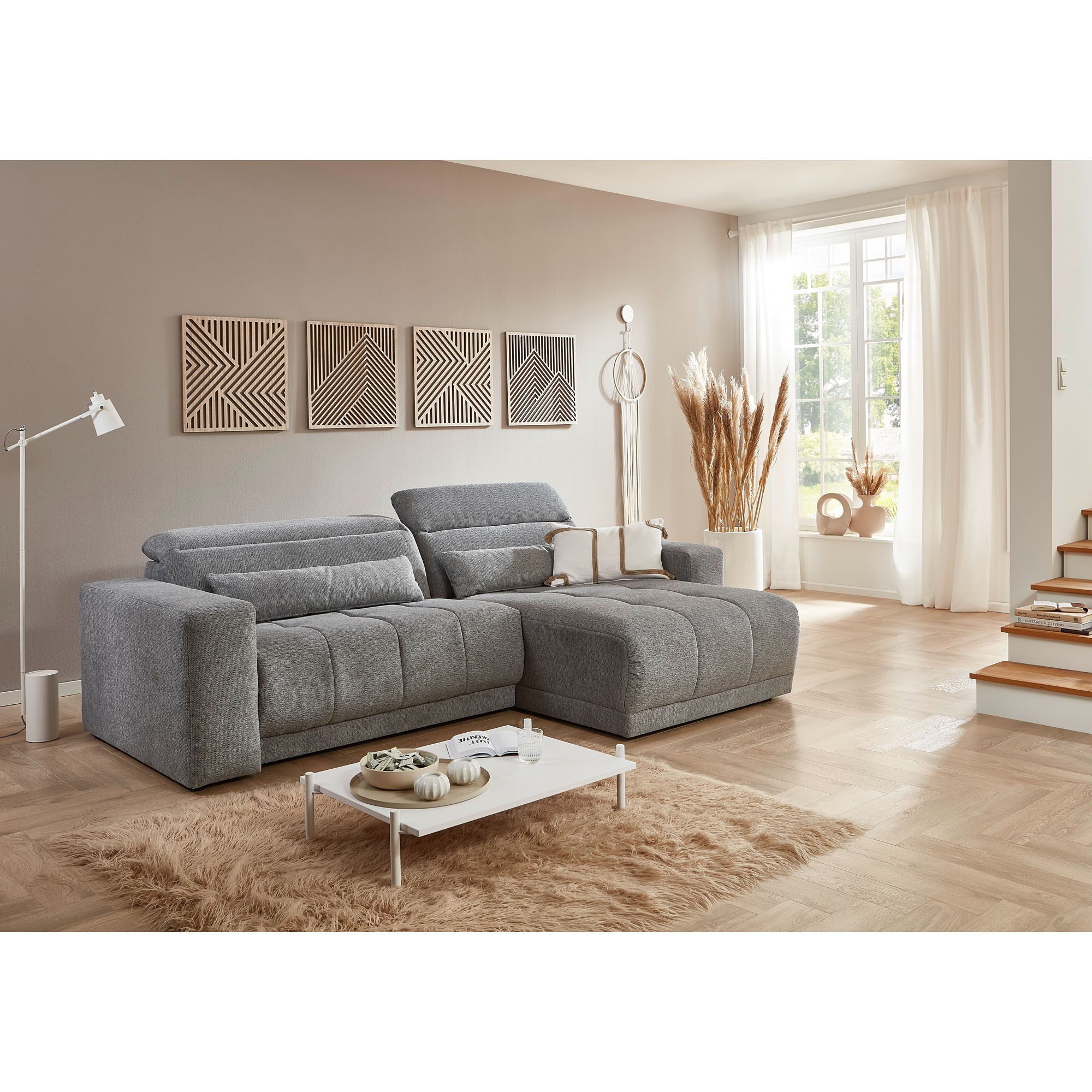Graues Ecksofa mit Ottomane und verstellbaren Rückenlehnen in einem hellen Wohnzimmer mit Couchtisch und Dekoration