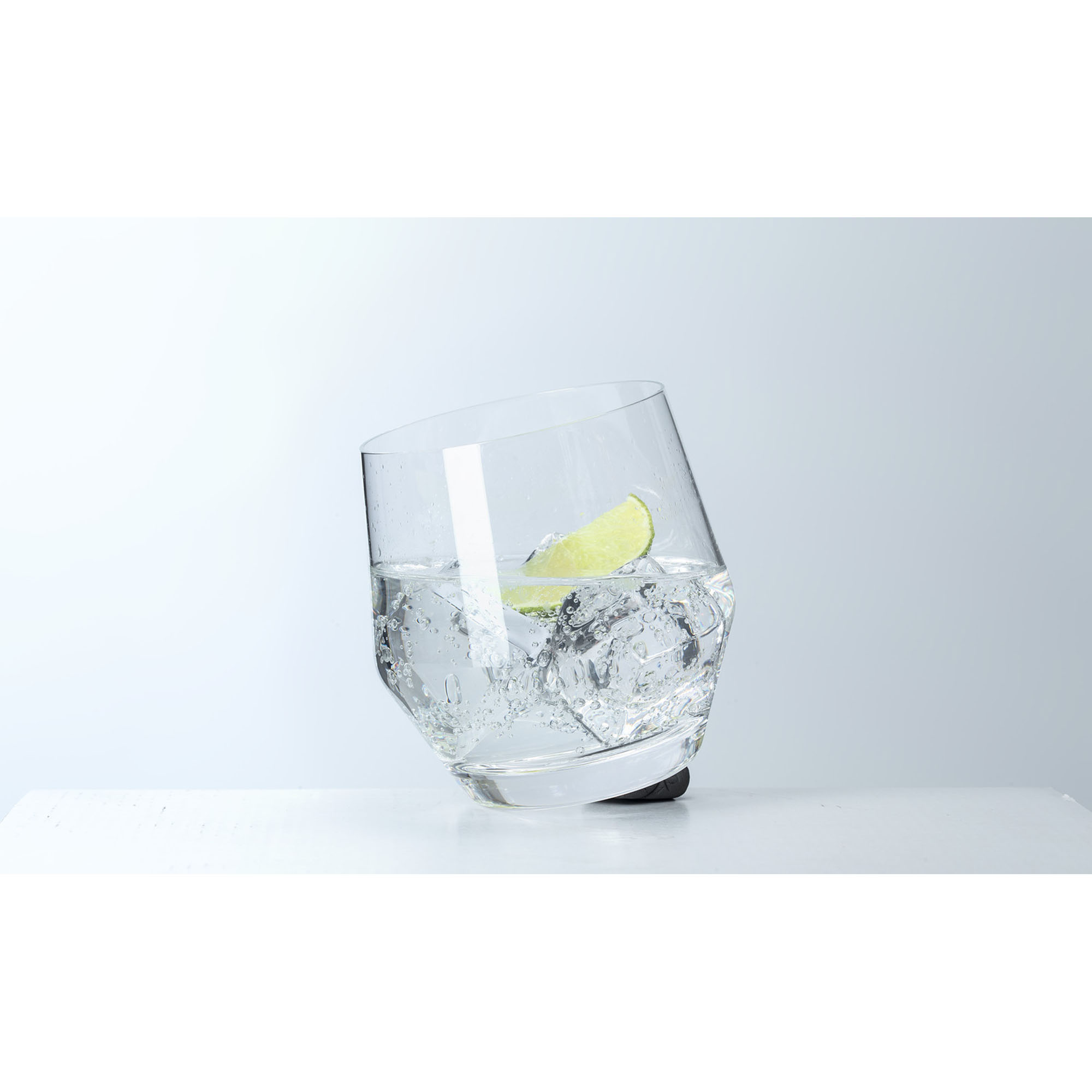 Schräg stehendes Trinkglas mit Eiswürfeln und Limettenscheibe