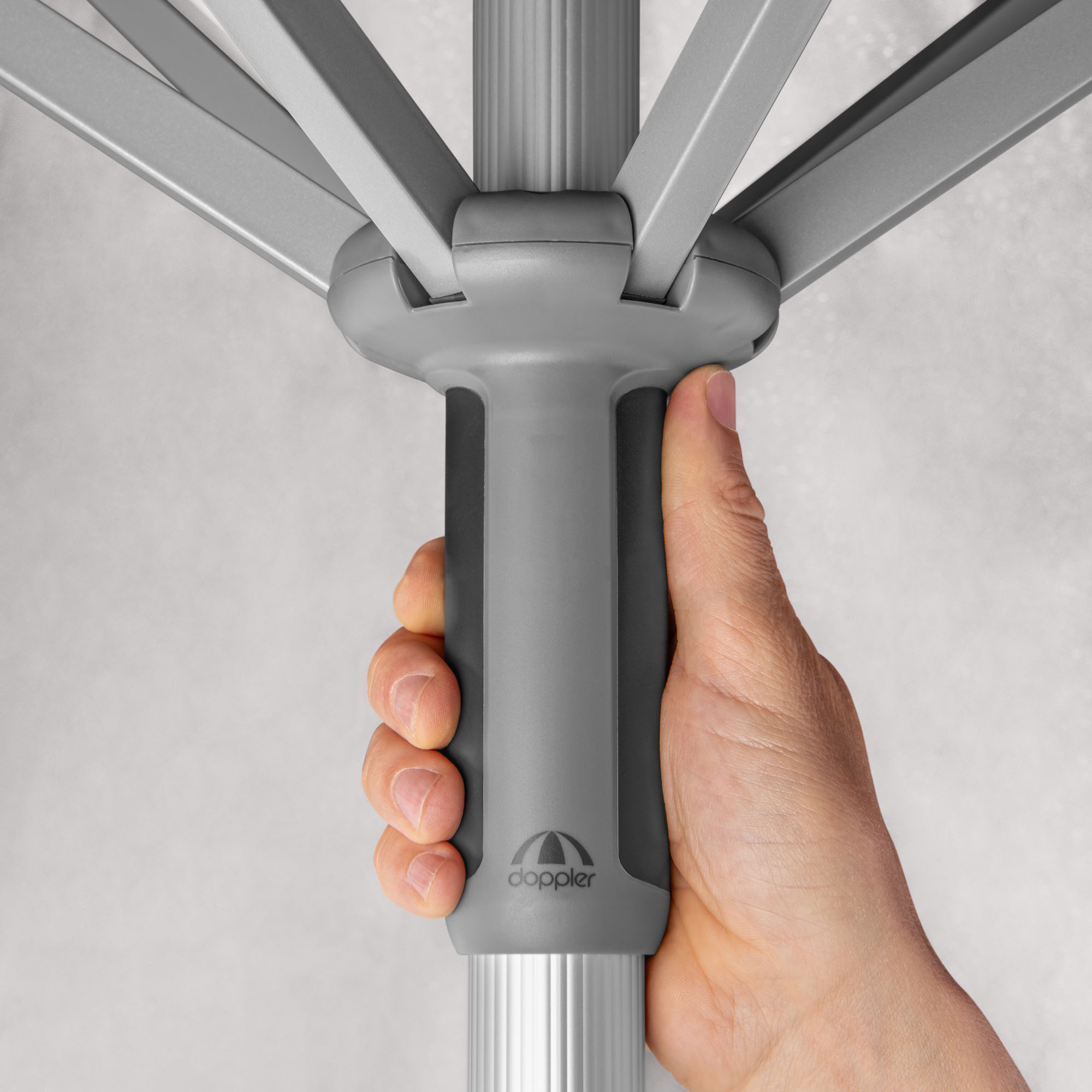 Nahaufnahme einer Hand, die den ergonomischen Griff am Mast des hellgrauen Sonnenschirms betätigt, stabile Streben sichtbar.