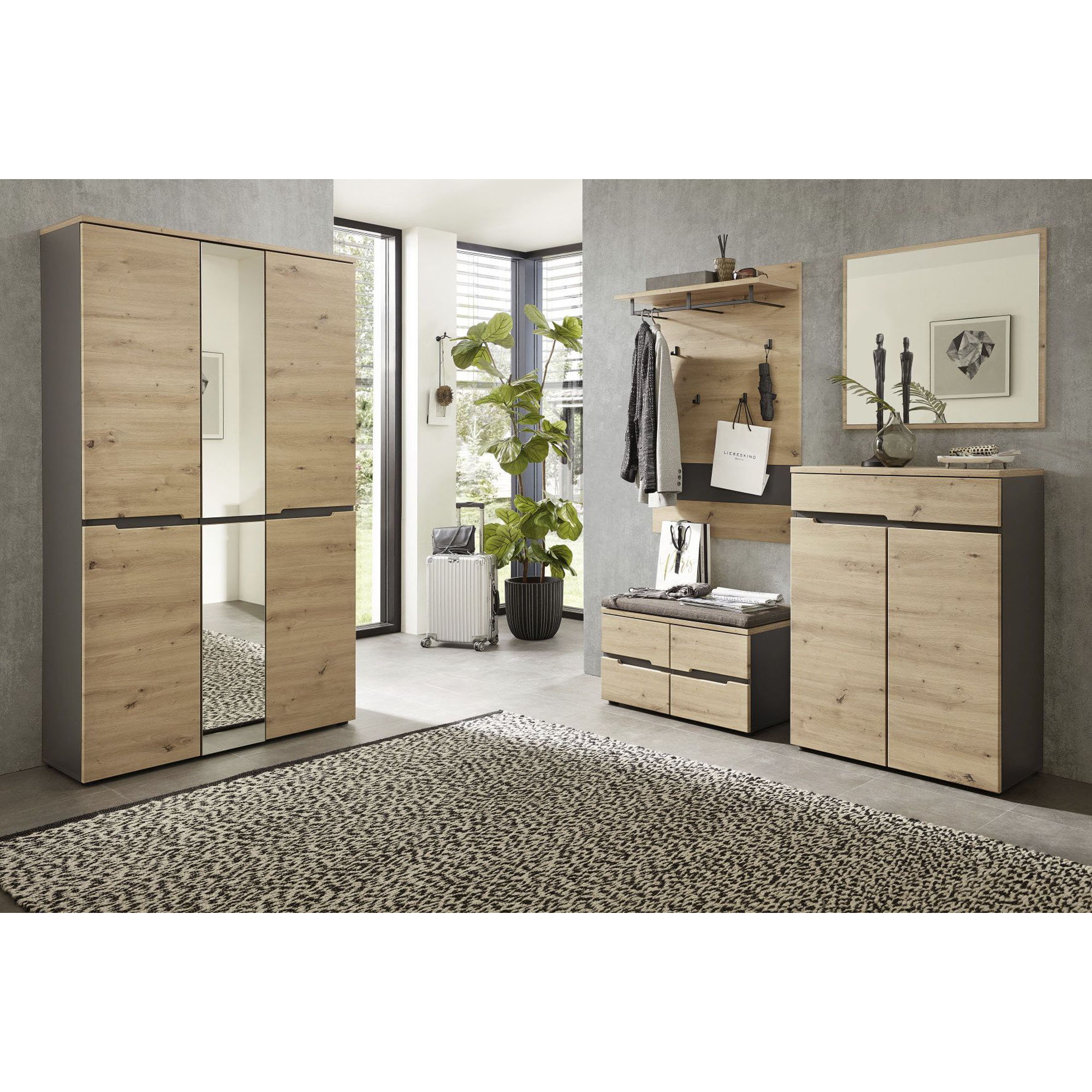 Raumaufnahme mit Garderobenmöbeln in Holzoptik, darunter ein hoher Schrank mit Spiegelelement, Wandpaneel, Spiegel und Kommode.