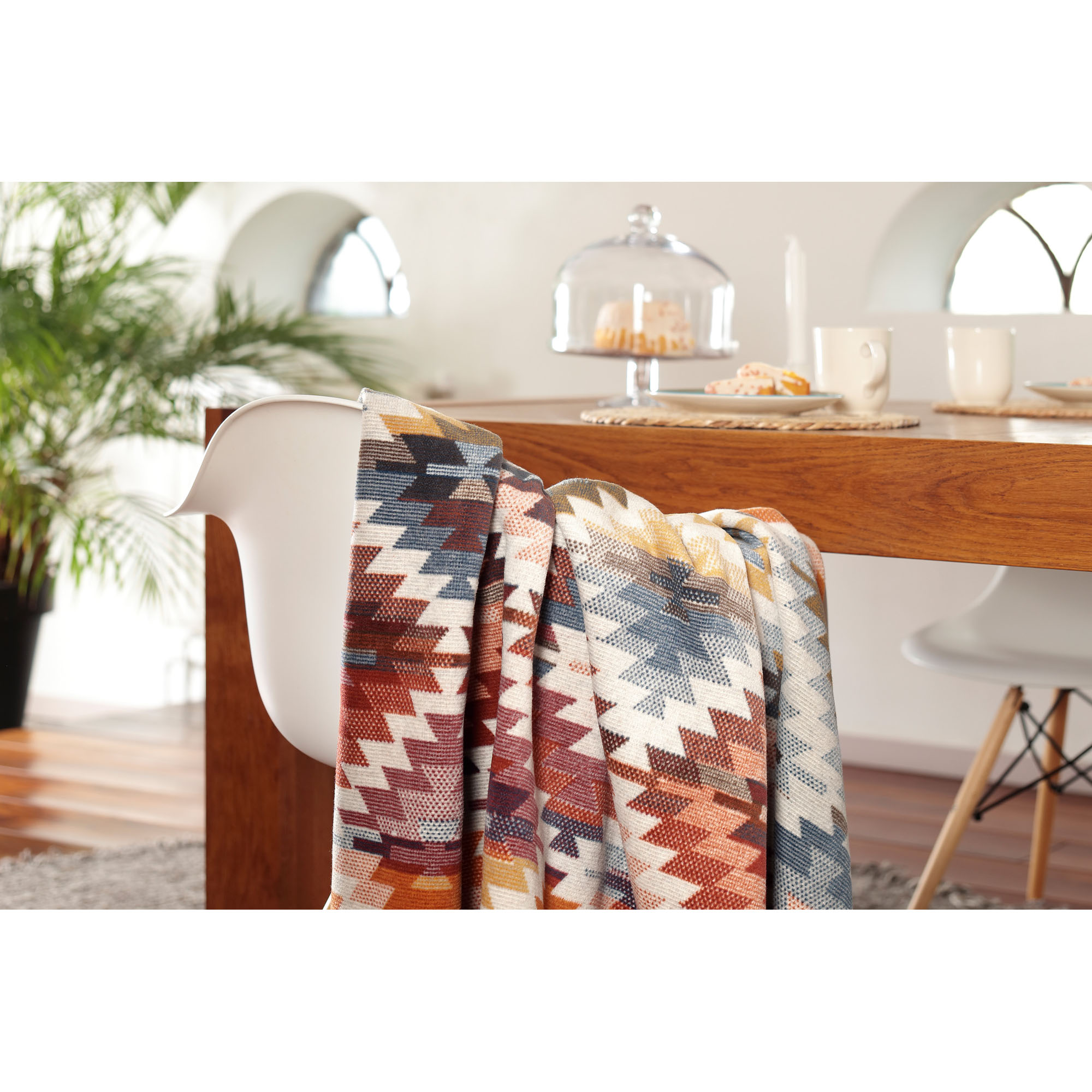 Wohndecke Nomad Light liegt locker über einer weißen Stuhllehne vor einem Holztisch.
