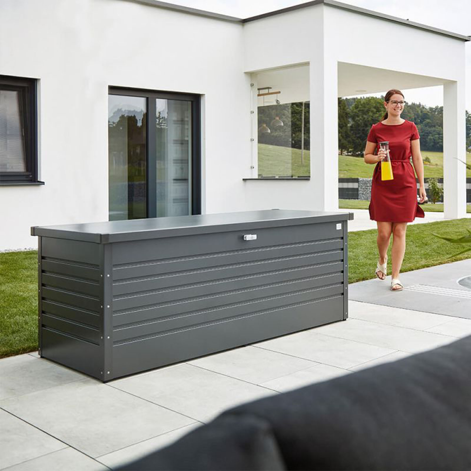 Graue Auflagenbox aus Metall auf einer gepflasterten Terrasse vor einem Wohnhaus