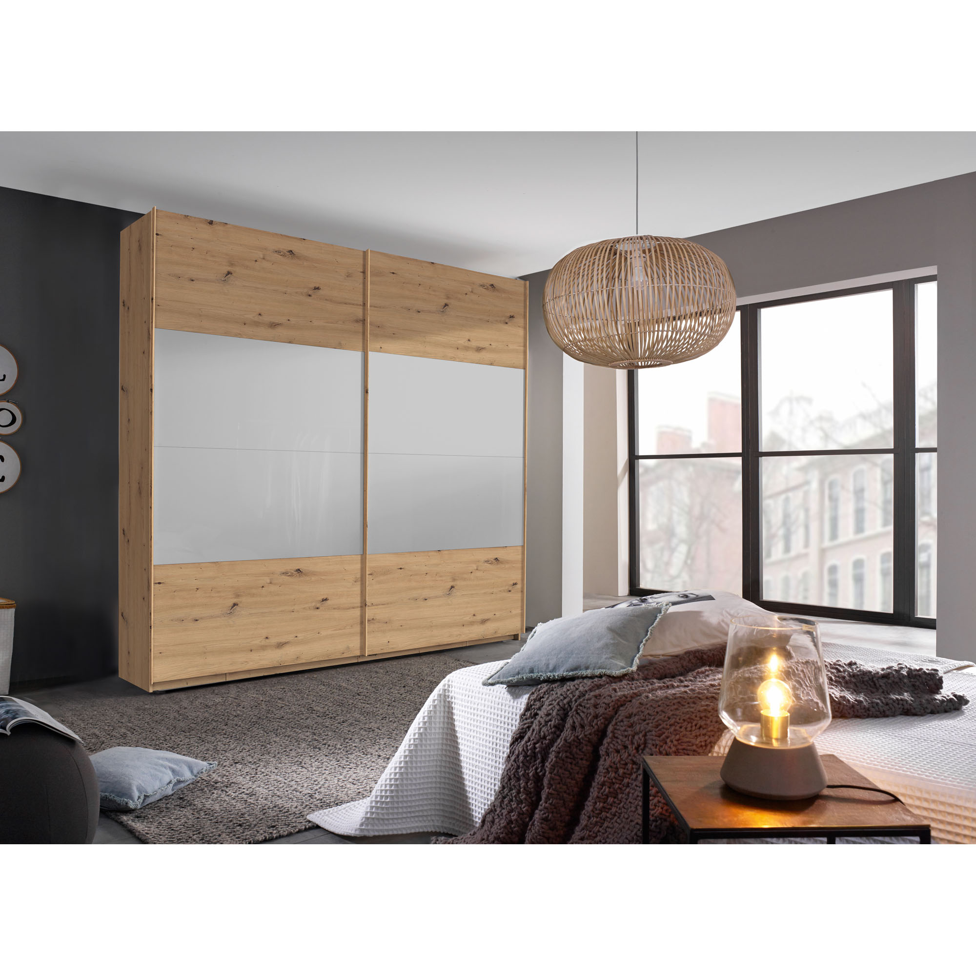 Schwebetürenschrank in Eiche Artisan mit Front in Seidengrau, in Schrägansicht in einem Schlafzimmer-Milieu gezeigt.