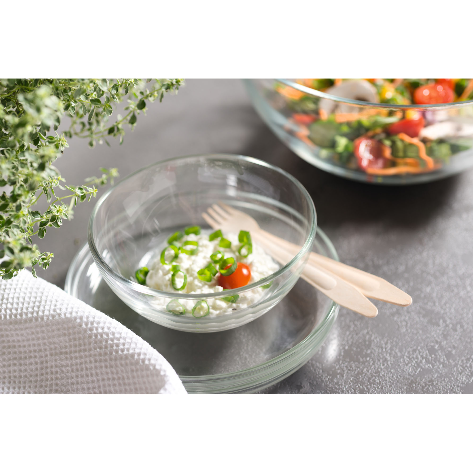 Kleine Glasschale mit cremigem Dip und Frühlingszwiebeln auf Glasplatte daneben Salat im Hintergrund