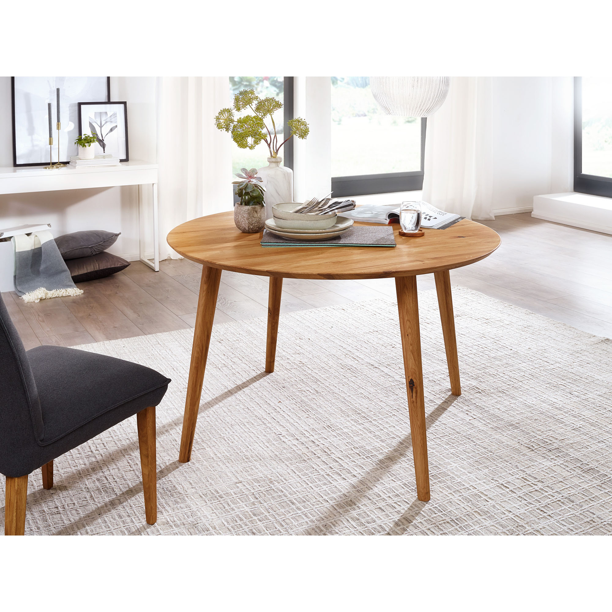 Runder Esstisch aus Holz mit Dekoration in einem hellen Esszimmer mit Teppich und Stuhl