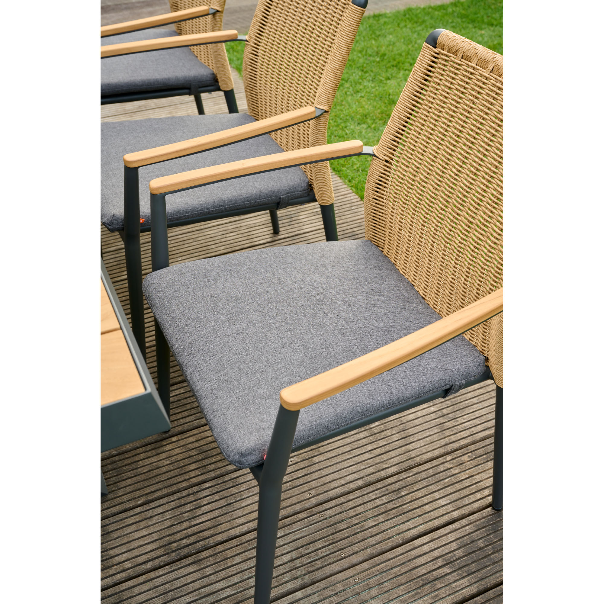 Gartenstuhl mit Polyrattan-Rückenlehne, Holzarmlehnen und dunkelgrauem Sitzpolster, auf einer Terrasse neben einem Tisch platziert