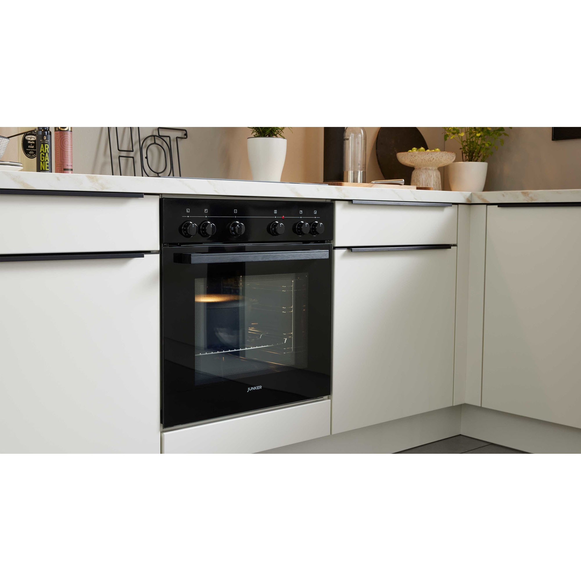 Schwarzer Einbau-Backofen in einer weißen Küchenzeile mit heller Arbeitsplatte und Dekoration aus Pflanzen und Küchenutensilien