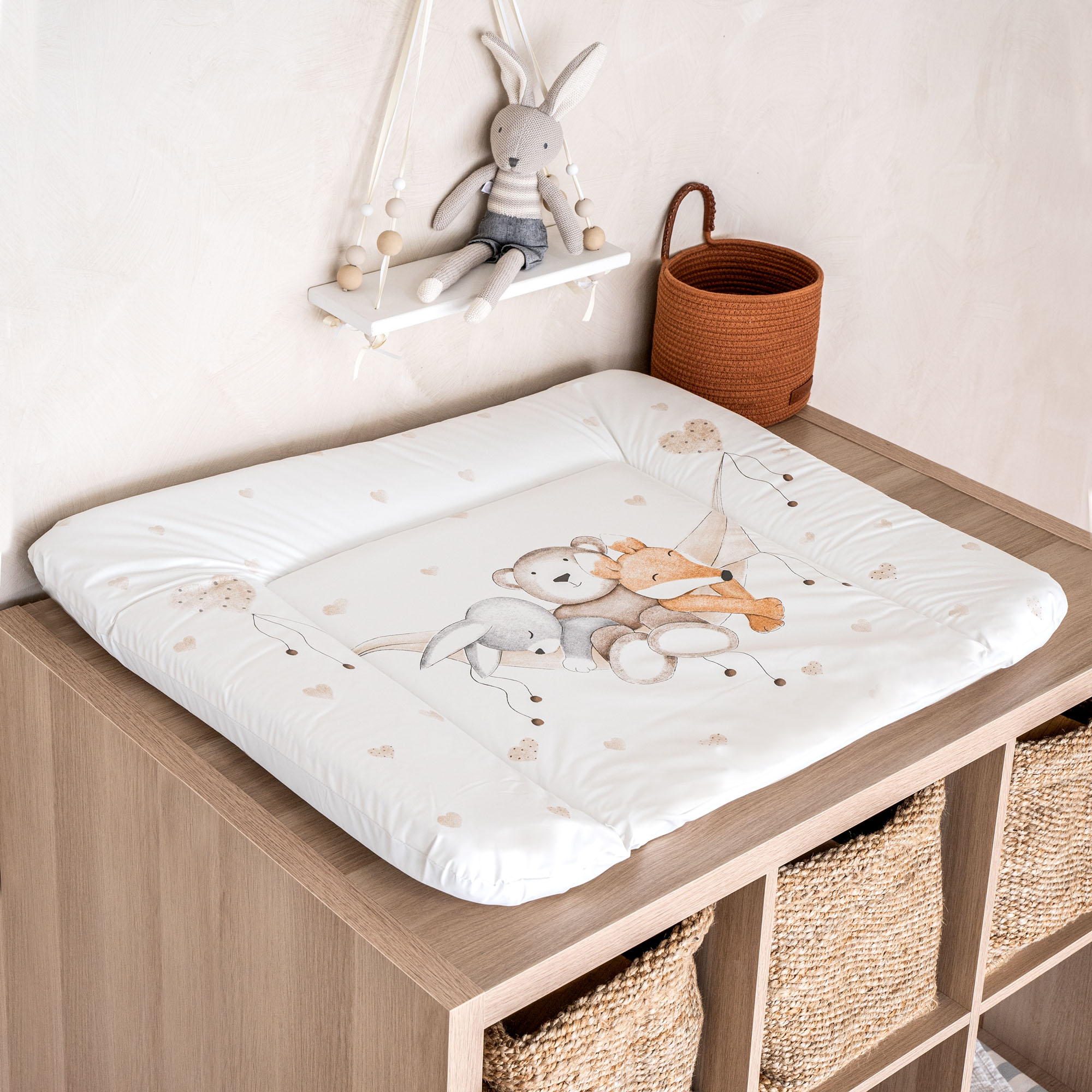 Das Bild zeigt eine Wickelauflage mit Tiermotiv auf einer Holzkommode mit Körben, daneben dekorative Elemente