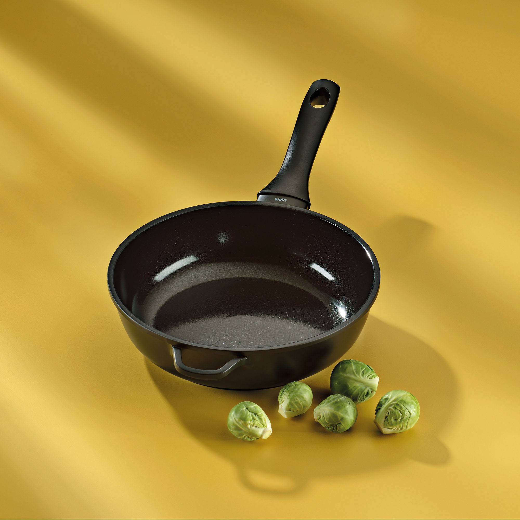 Schwarze Schmorpfanne mit Stielgriff auf gelbem Hintergrund neben grünen Tomaten
