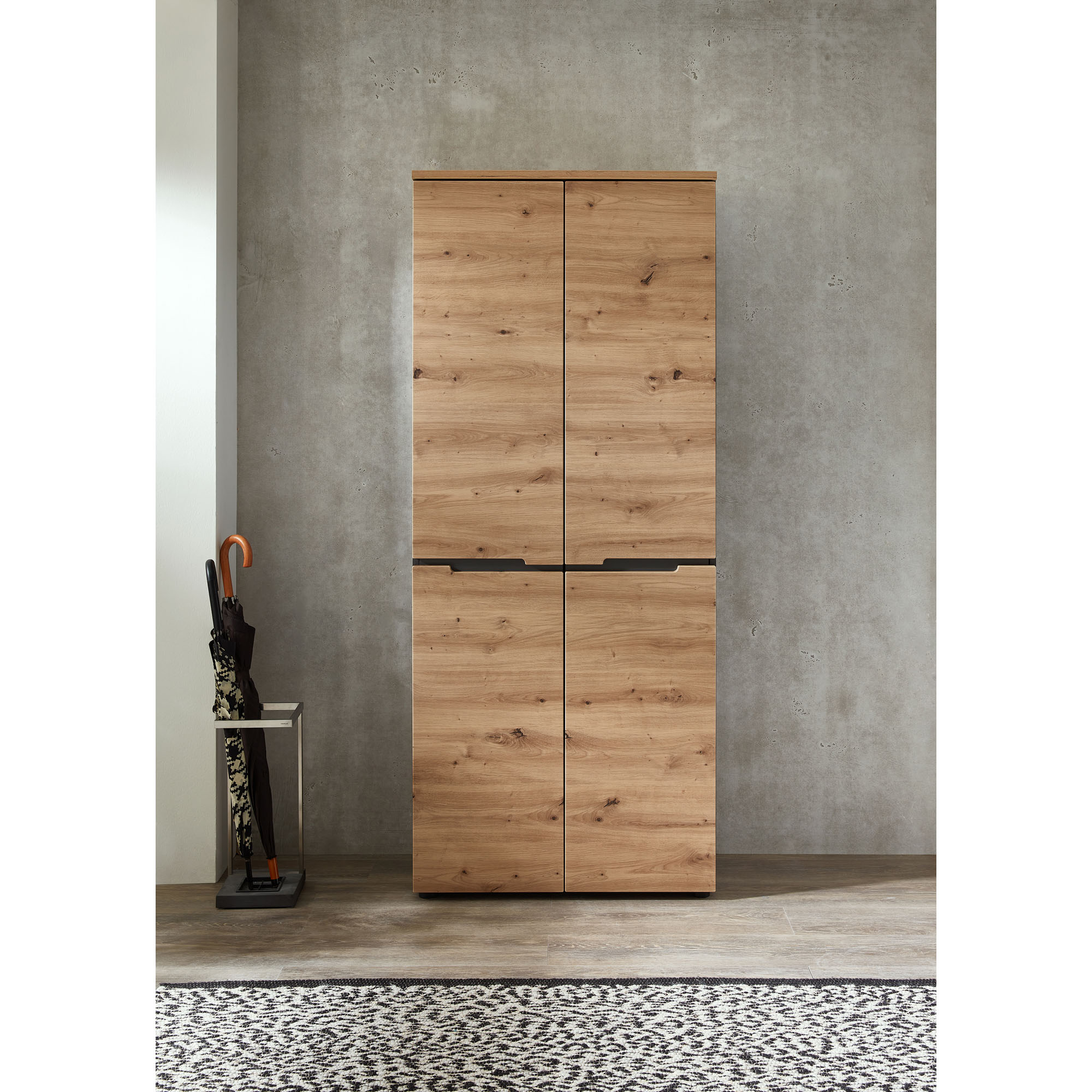 Geschlossener hoher Schrank in Holzoptik, frontal vor grauer Wand im Flur aufgenommen.