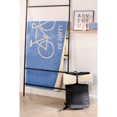 Blaues Travel-Strandtuch mit Fahrradmotiv hängt über einer schwarzen Leiter in einer hellen Raumszene.