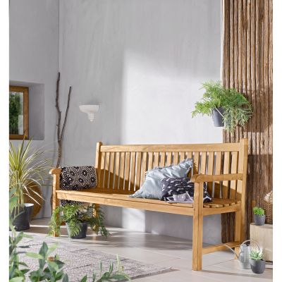 Sitzbank aus Holz mit Rückenlehne und Armlehnen in einem Wohnraum mit Pflanzen und Kissen