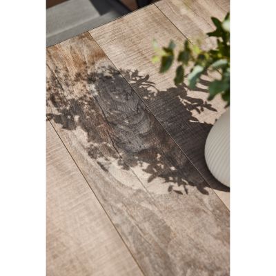 Tischplatte in Holzoptik mit Licht- und Schattenspiel durch Pflanzen auf der Oberfläche.