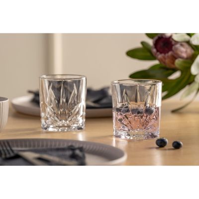 Zwei transparente Whiskygläser mit facettierter Struktur auf gedecktem Tisch mit Beeren