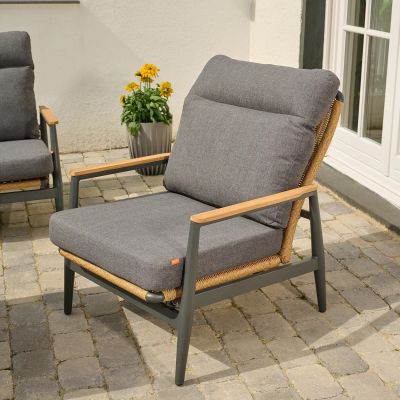 Ein Sessel mit dunklem Gestell, seitlich sichtbarem Geflecht und grauen Sitz- und Rückenpolstern, auf einer Terrasse platziert.