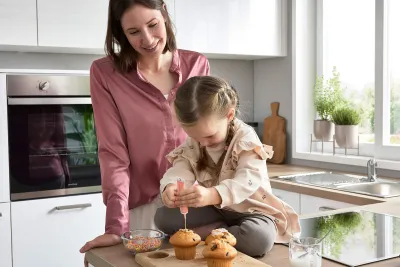 Mutter und Kind beim Muffins backen in weißer Hochglanzküche mit Holzarbeitsfläche