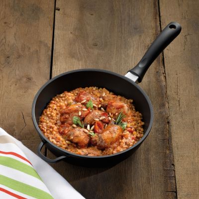 Schmorpfanne mit zubereitetem Gericht aus Tomaten Gemüse und Kräutern auf einer dunklen Holzfläche