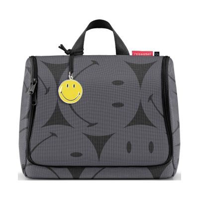 Kulturbeutel von Reisenthel, Modell Toiletbag XL, in Grau mit großflächigem Smiley-Muster, frontal geschlossen mit Tragegriff und Smiley-Anhänger.