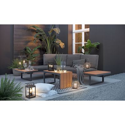 Gartensofa mit Polstern und niedriger Tisch auf einer Terrasse mit Pflanzen und Beleuchtung im Hintergrund