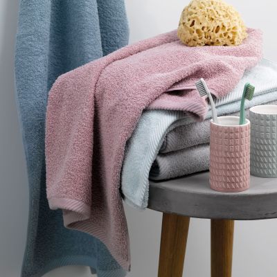 Altrosafarbenes Badtextil auf einem kleinen Beistelltisch neben Behältern Bürste und gelbem Badeschwamm