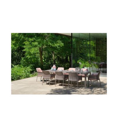 Eine moderne Terrasse mit mehreren taupefarbenen Stühlen und einem rechteckigen Esstisch. Auf dem Tisch stehen Geschirr, Gläser und Dekoration, im Hintergrund sind grüne Bäume und Glaswände zu sehen.